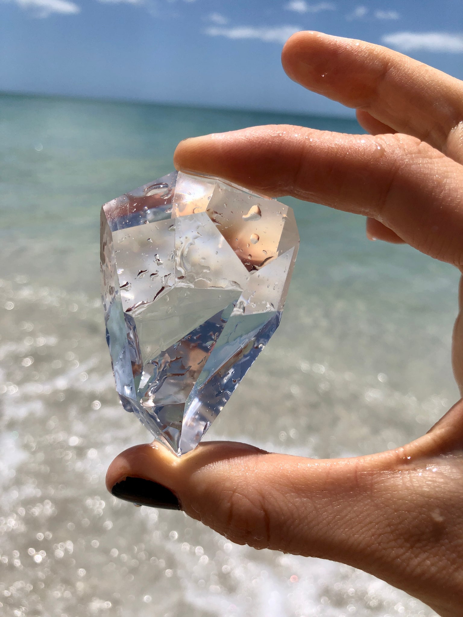 Faceted clear quartz freeform held in a hand at the beach