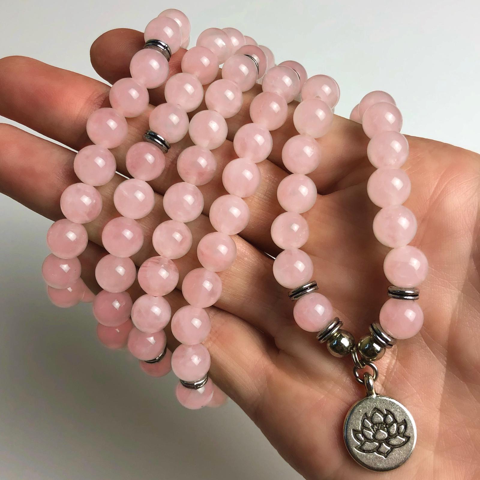 Rose quartz mala with pink beads and a lotus charm held in a hand